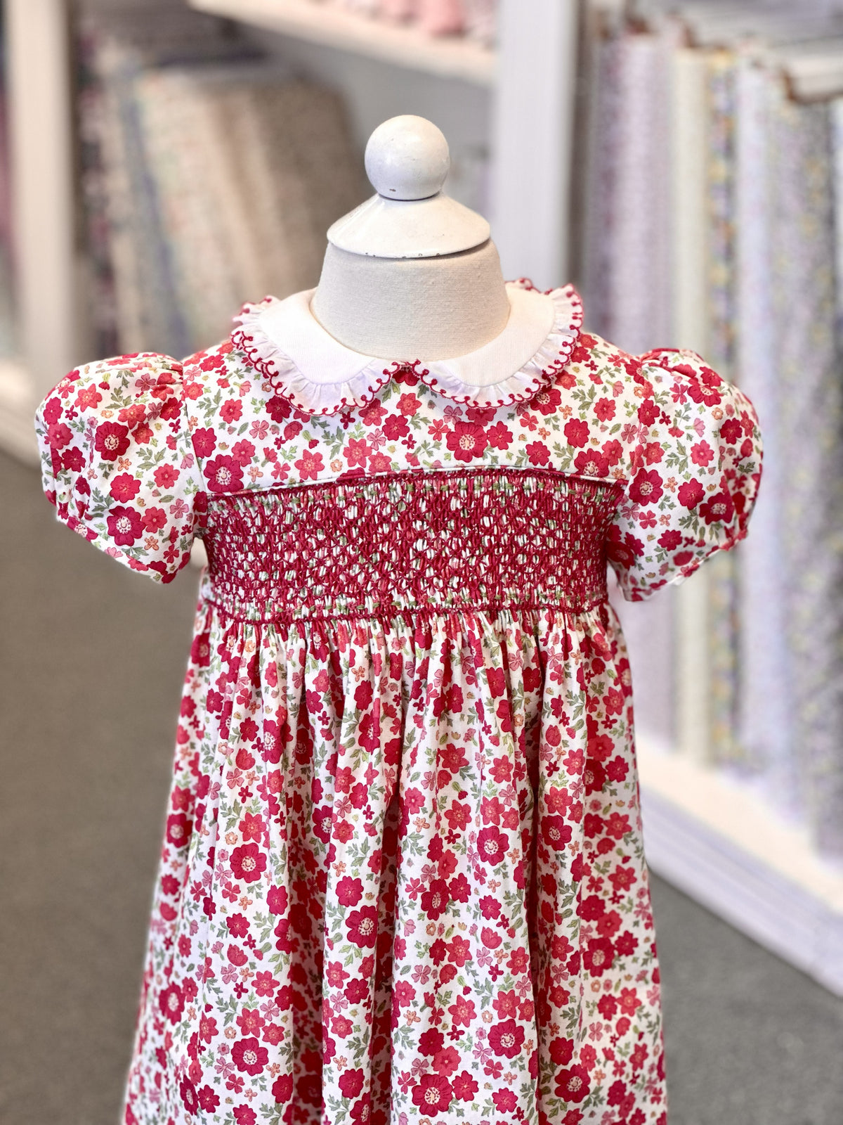 Red floral smocked girls dress with puff sleeves and white peter pan collar on mannequin