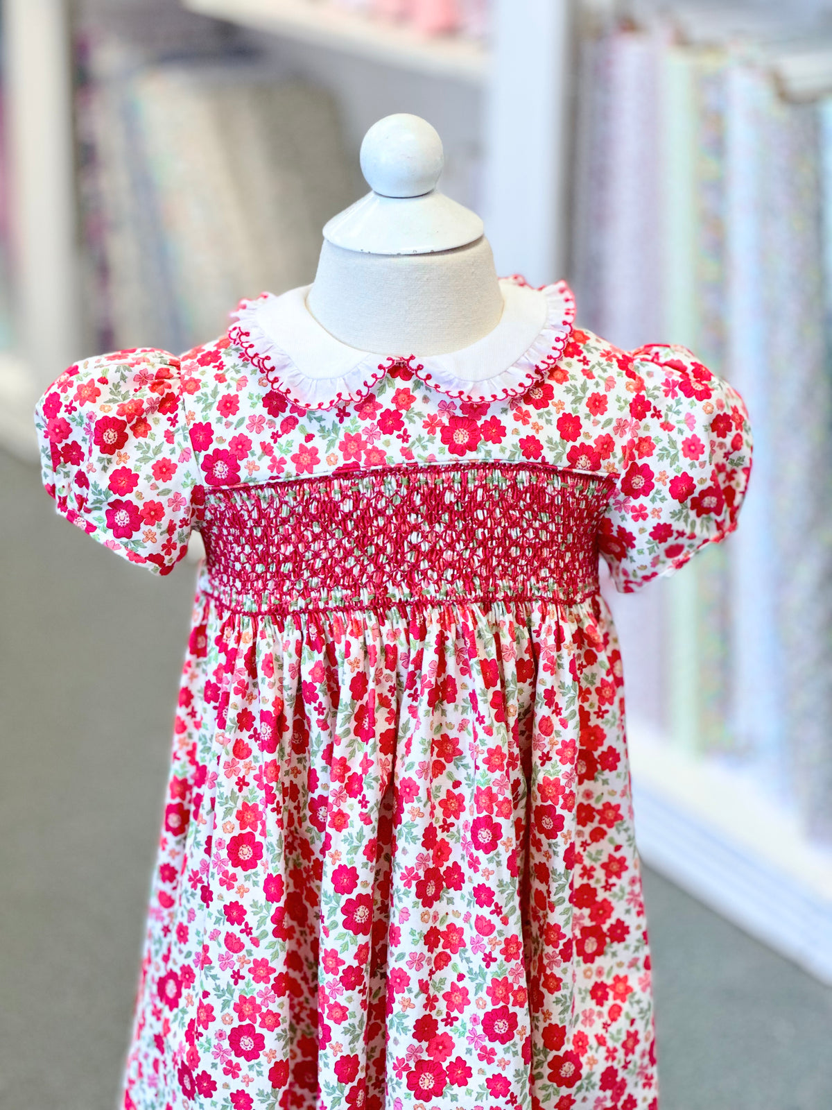 Child's smocked floral dress in red and pink on a white mannequin