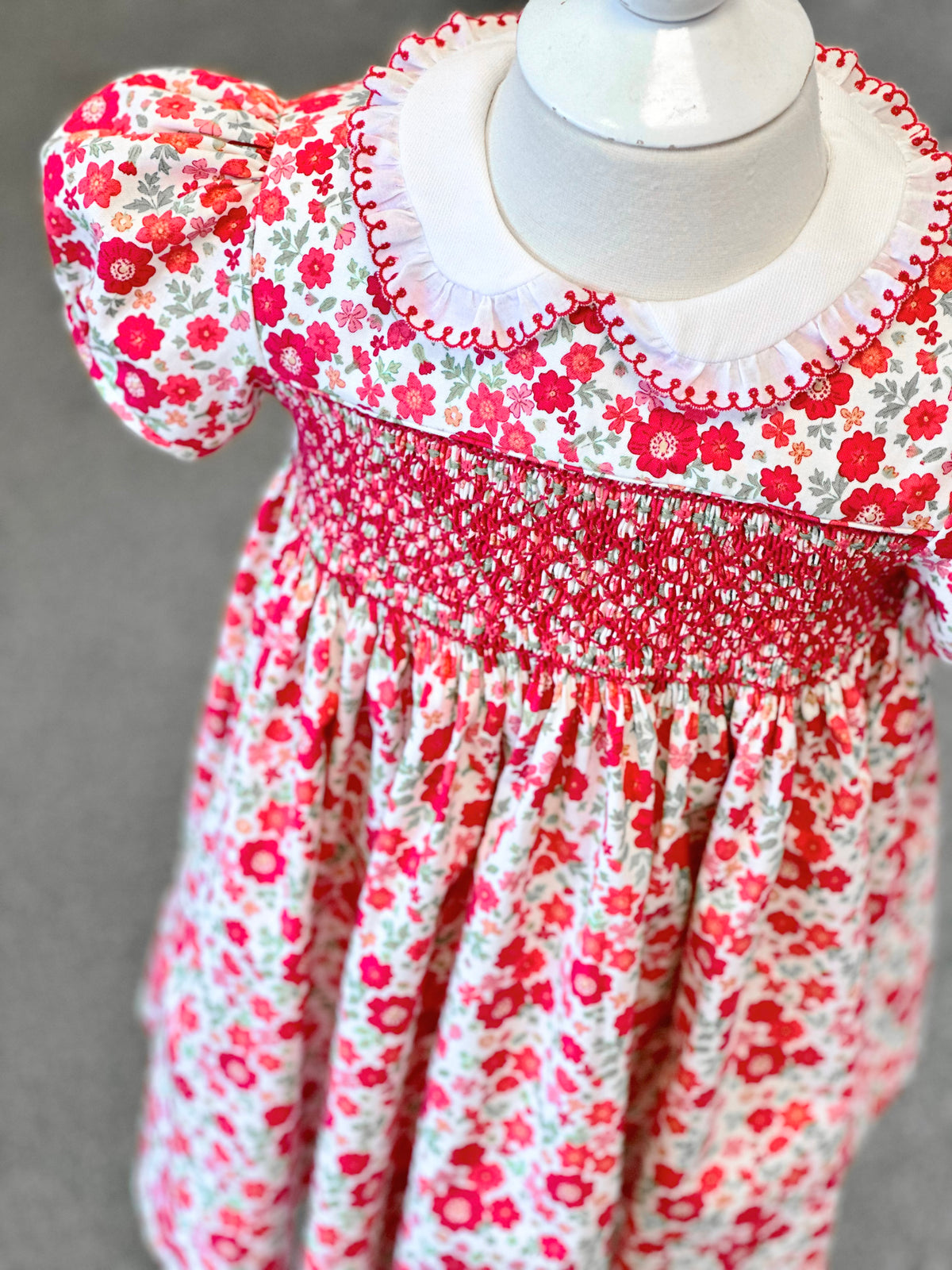 Red floral smocked toddler dress with white ruffle collar and puff sleeves on mannequin