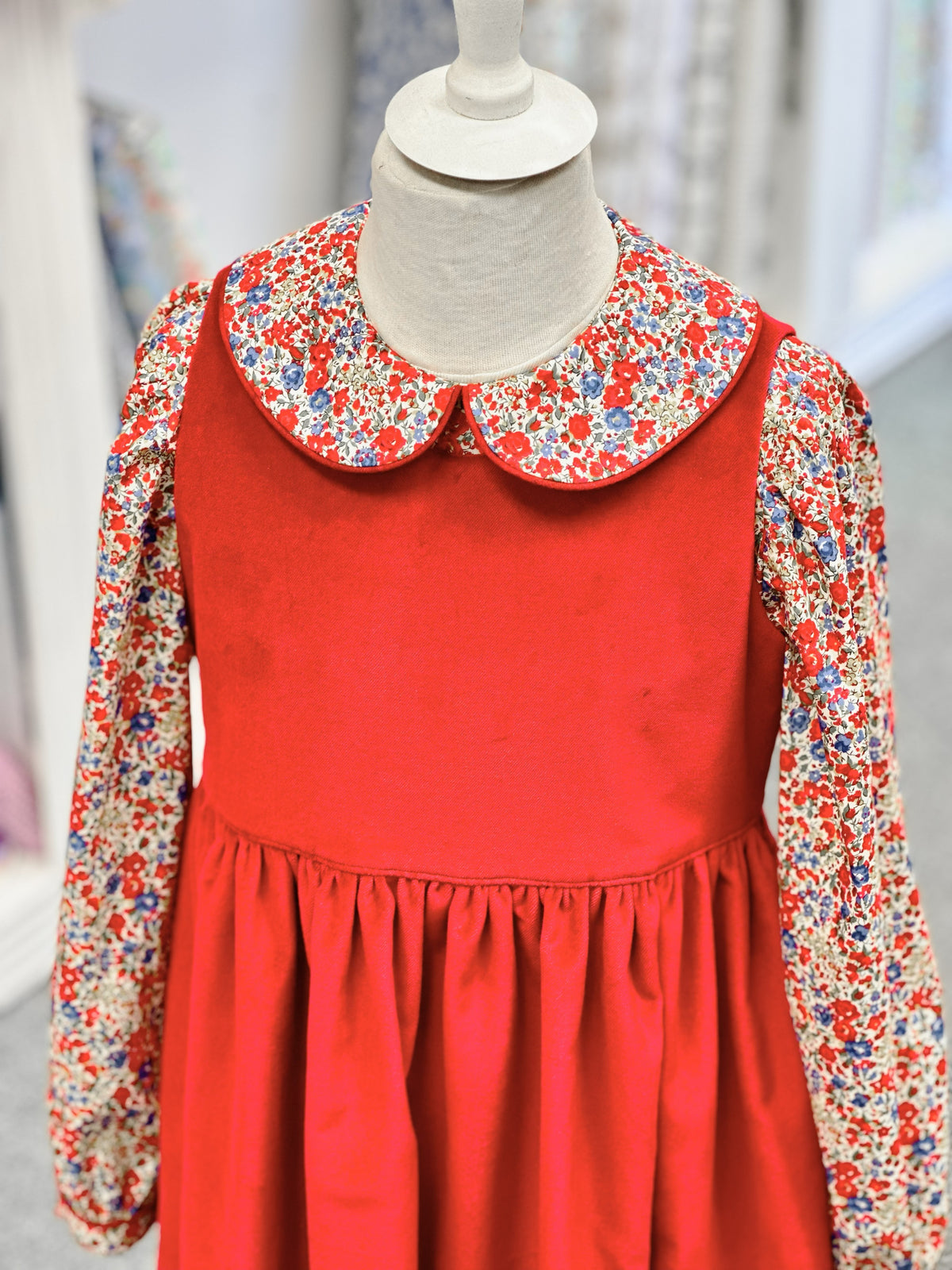 Red children's pinafore dress with floral Peter Pan collar blouse on mannequin