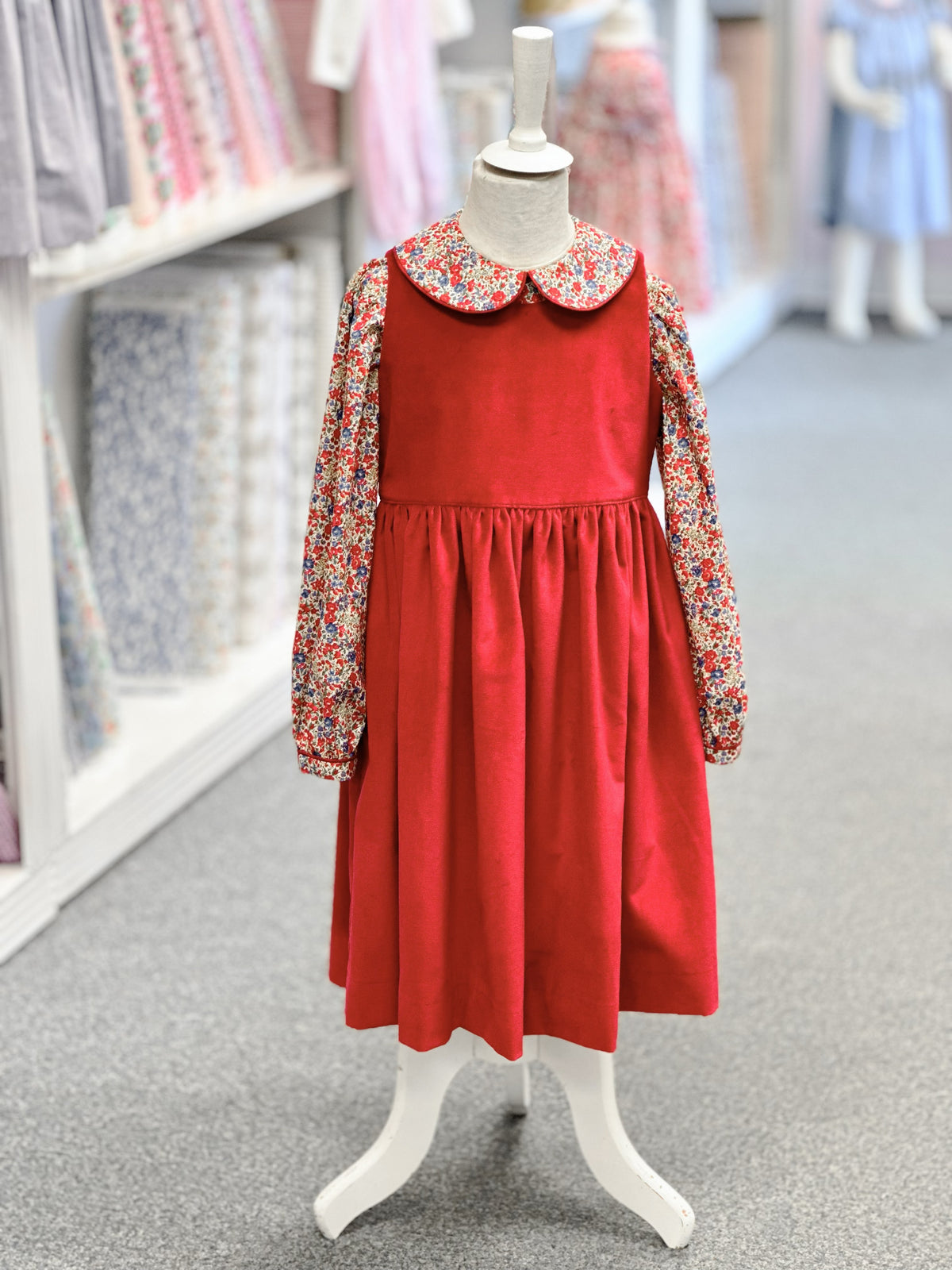 Red corduroy pinafore dress over floral long-sleeve blouse with Peter Pan collar on child mannequin