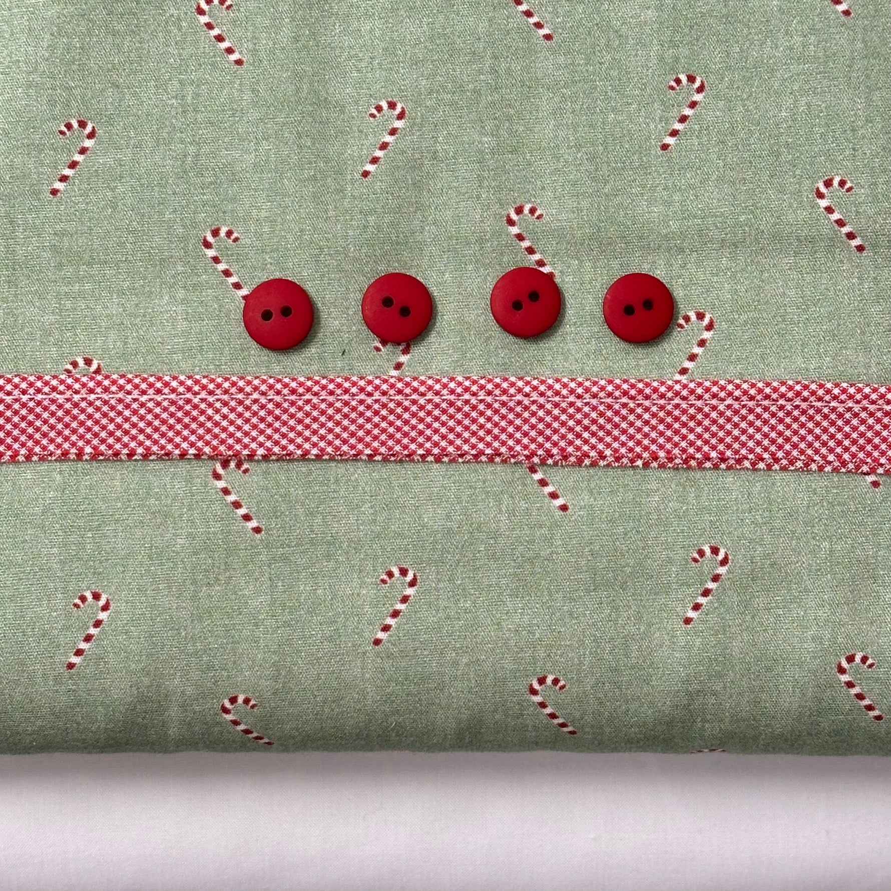 Green candy cane print fabric with red ribbon trim and four red buttons