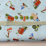 Light blue fabric with colorful construction vehicles, green gingham trim, and four green buttons