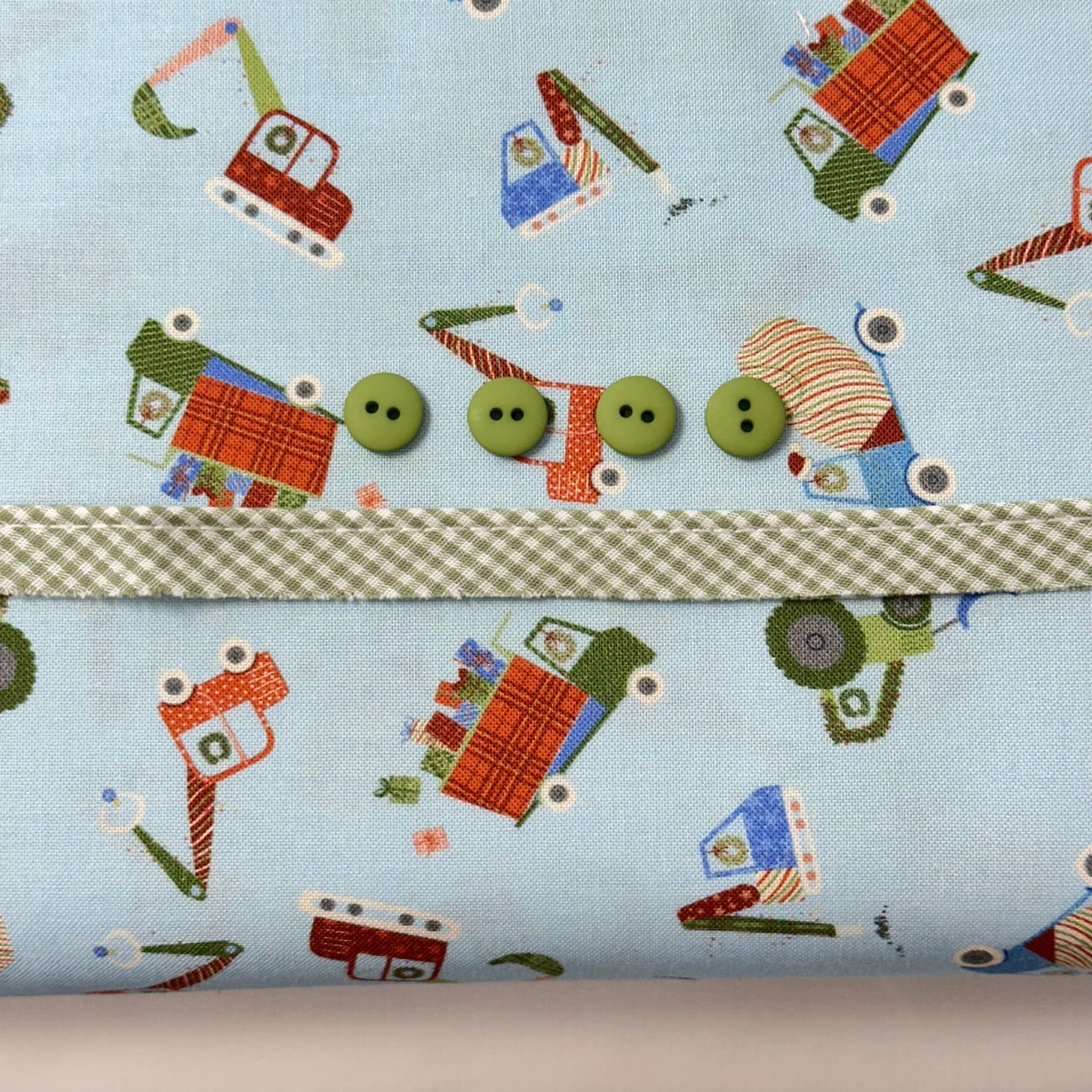 Light blue fabric with colorful construction vehicles, green gingham trim, and four green buttons