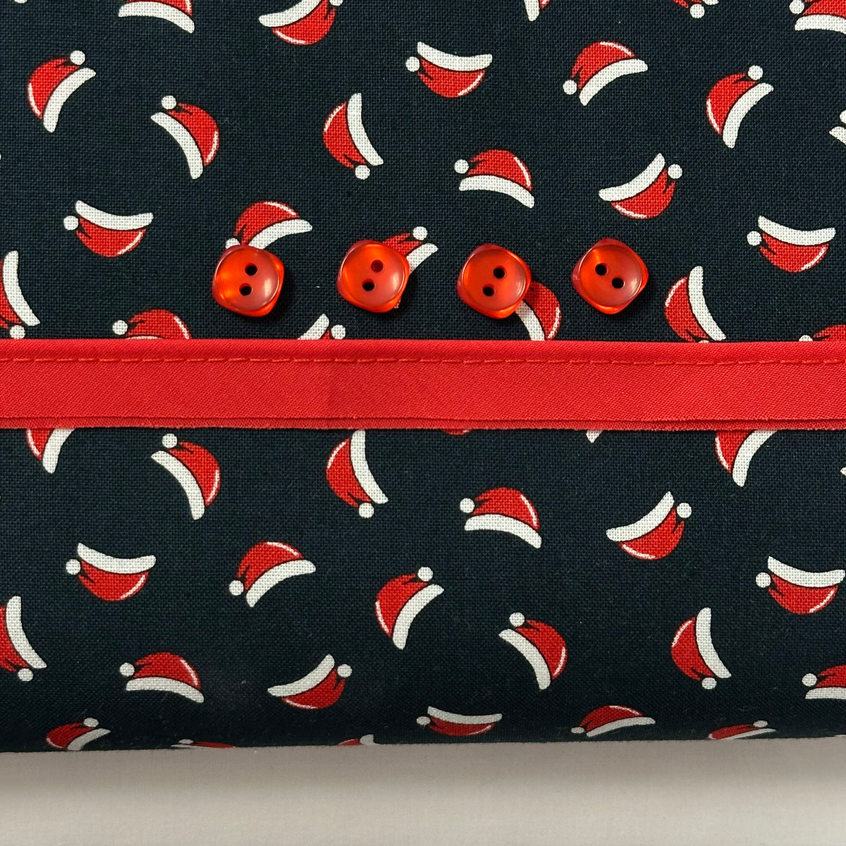 Navy fabric with Santa hat print, red ribbon trim, and four red buttons