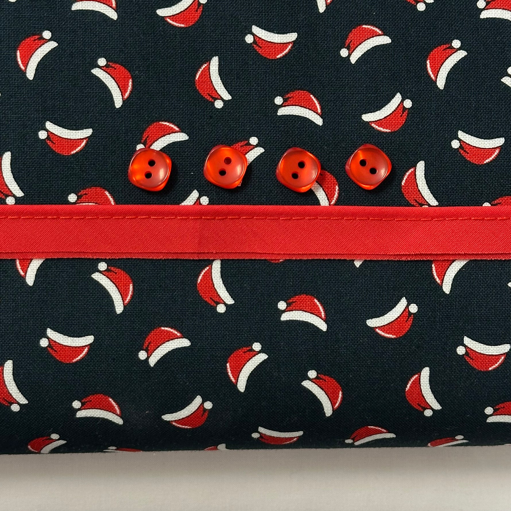 Navy fabric with Santa hat print, red ribbon trim, and four red buttons