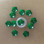 Shiny green flower-shaped plastic buttons with two holes, arranged in a circle