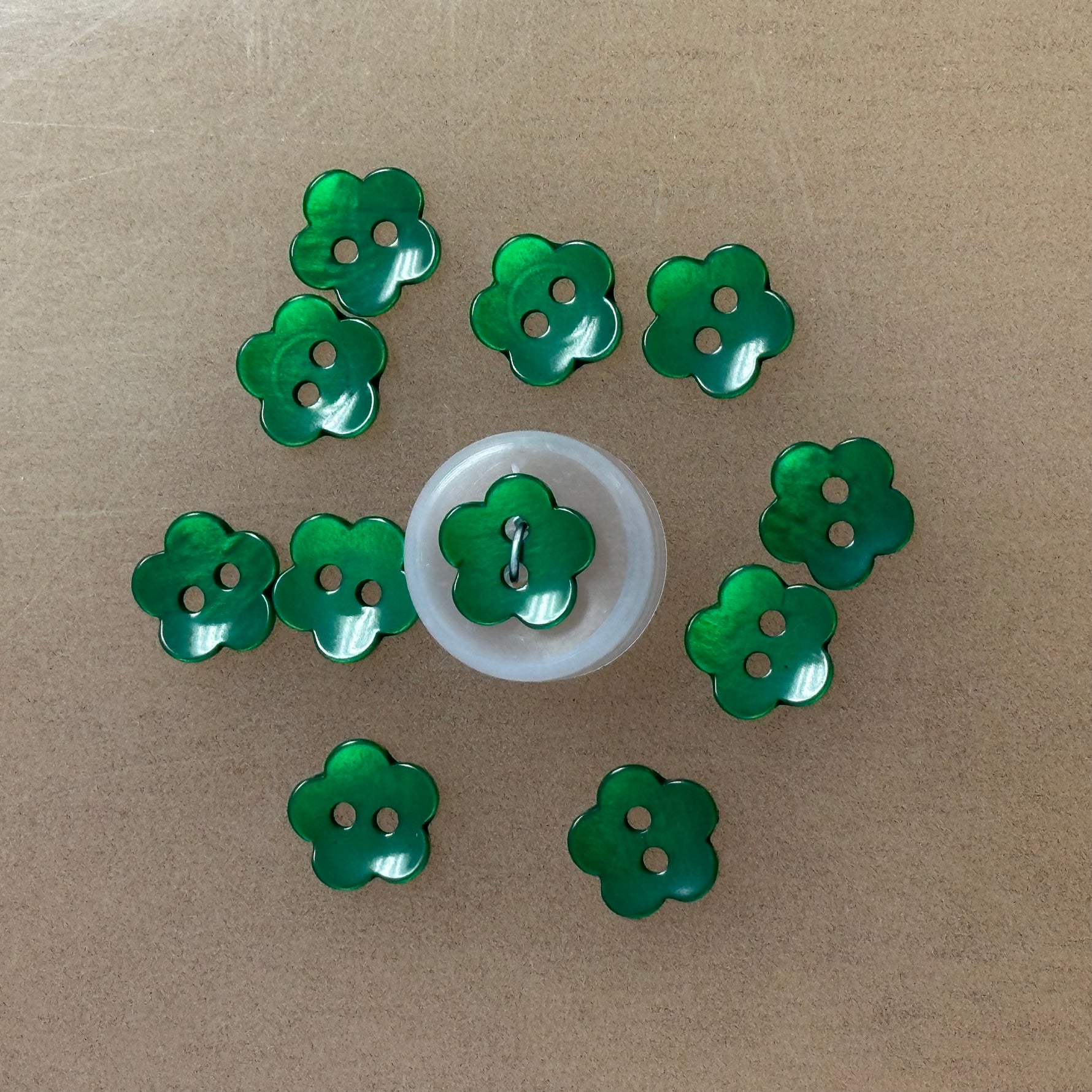 Shiny green flower-shaped plastic buttons with two holes, arranged in a circle