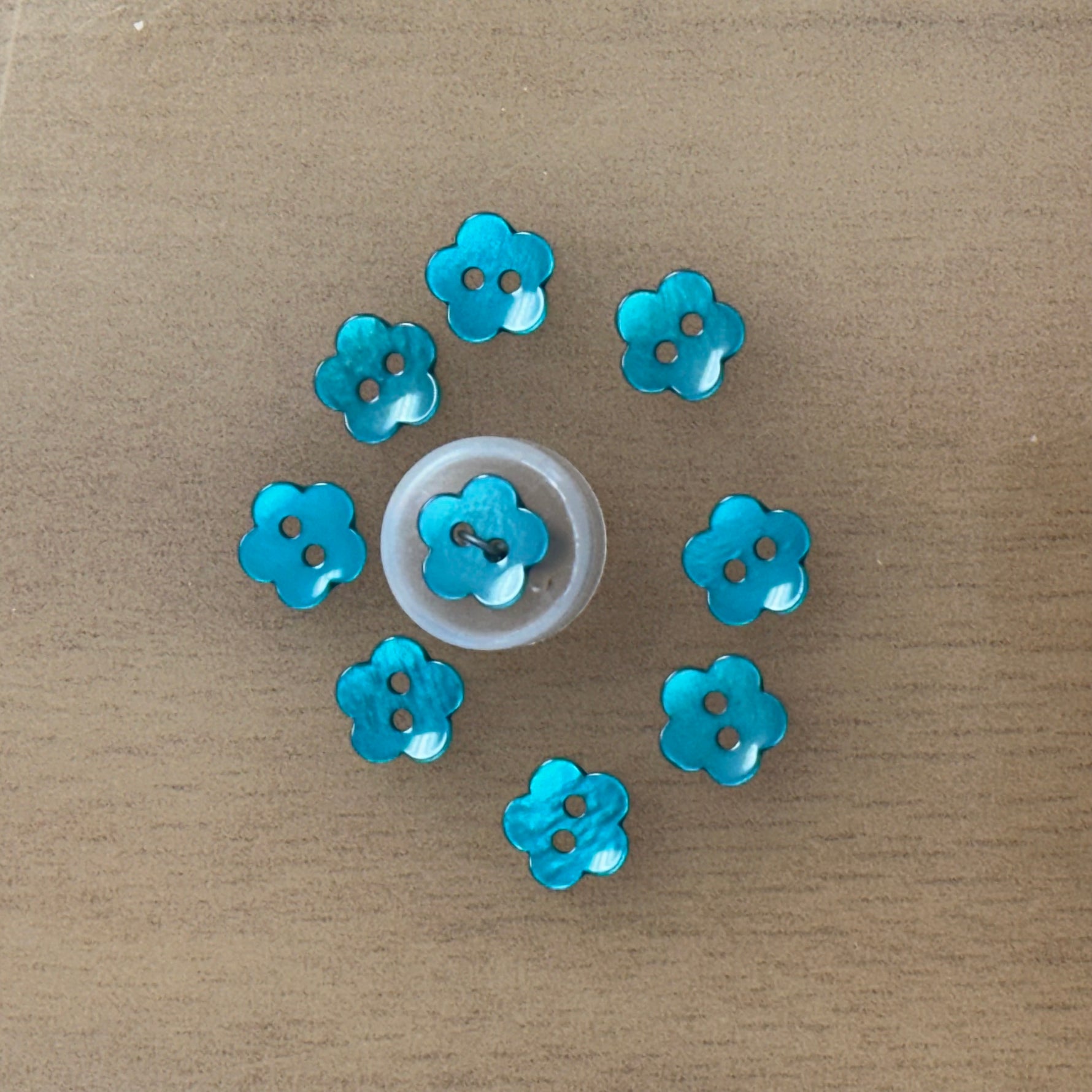 Teal blue flower-shaped two-hole plastic buttons arranged in a circle, 9 total