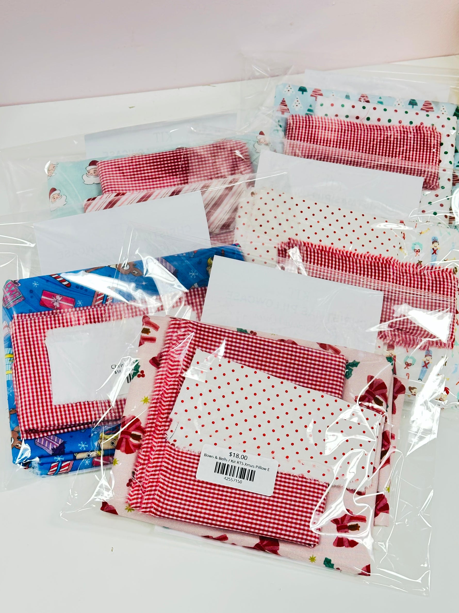 Christmas pillowcase kits in festive red gingham and holiday print fabrics, packaged in clear bags