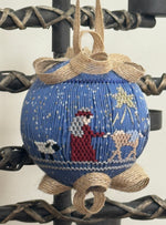 Blue smocked ornament with nativity scene, burlap bow, hanging on black iron stand