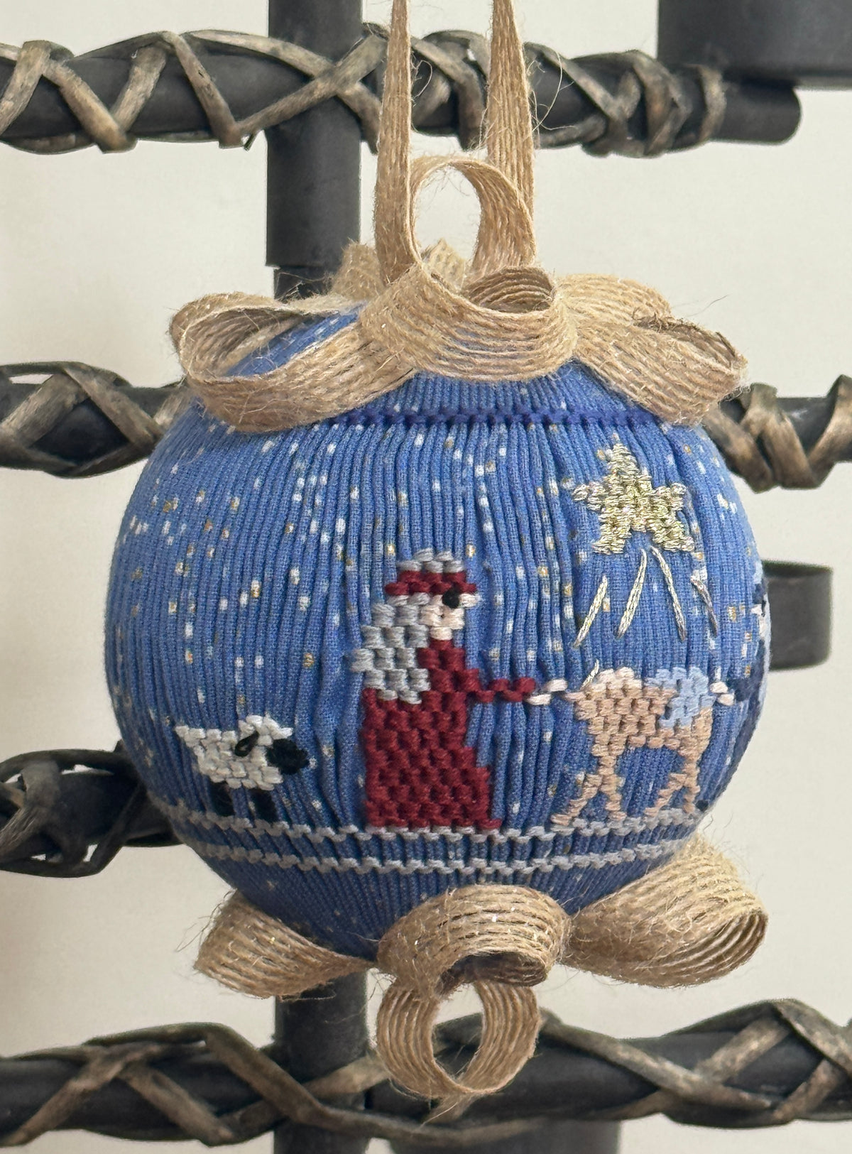 Blue smocked ornament with nativity scene, burlap bow, hanging on black iron stand