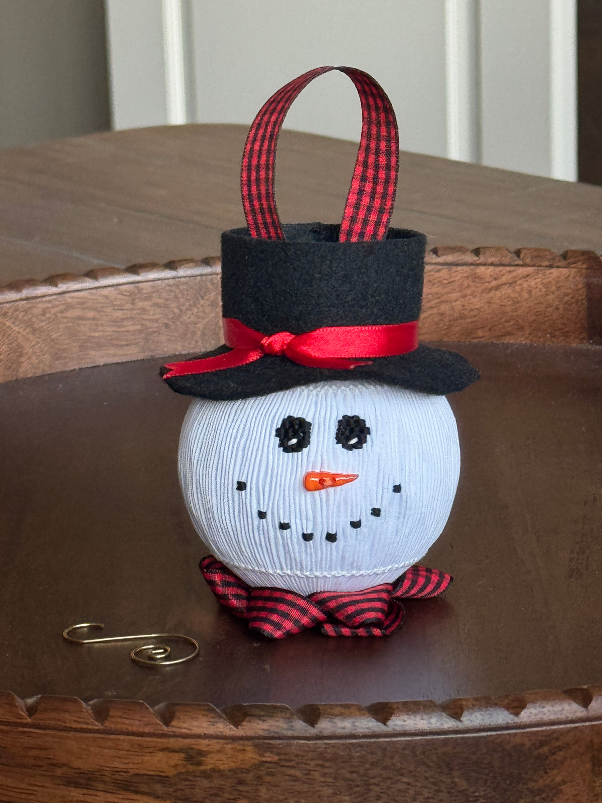 Smocked white snowman ornament with black top hat, red plaid bow and ribbon handle