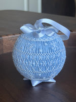 Light blue smocked fabric ornament ball with satin bow and ribbon hanger on display stand
