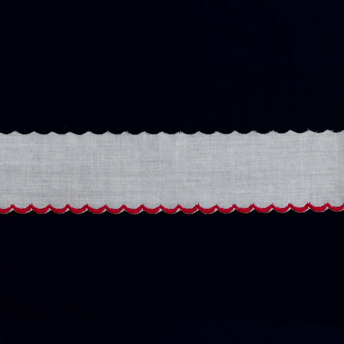 White cotton edging trim with red scalloped embroidered border on dark background