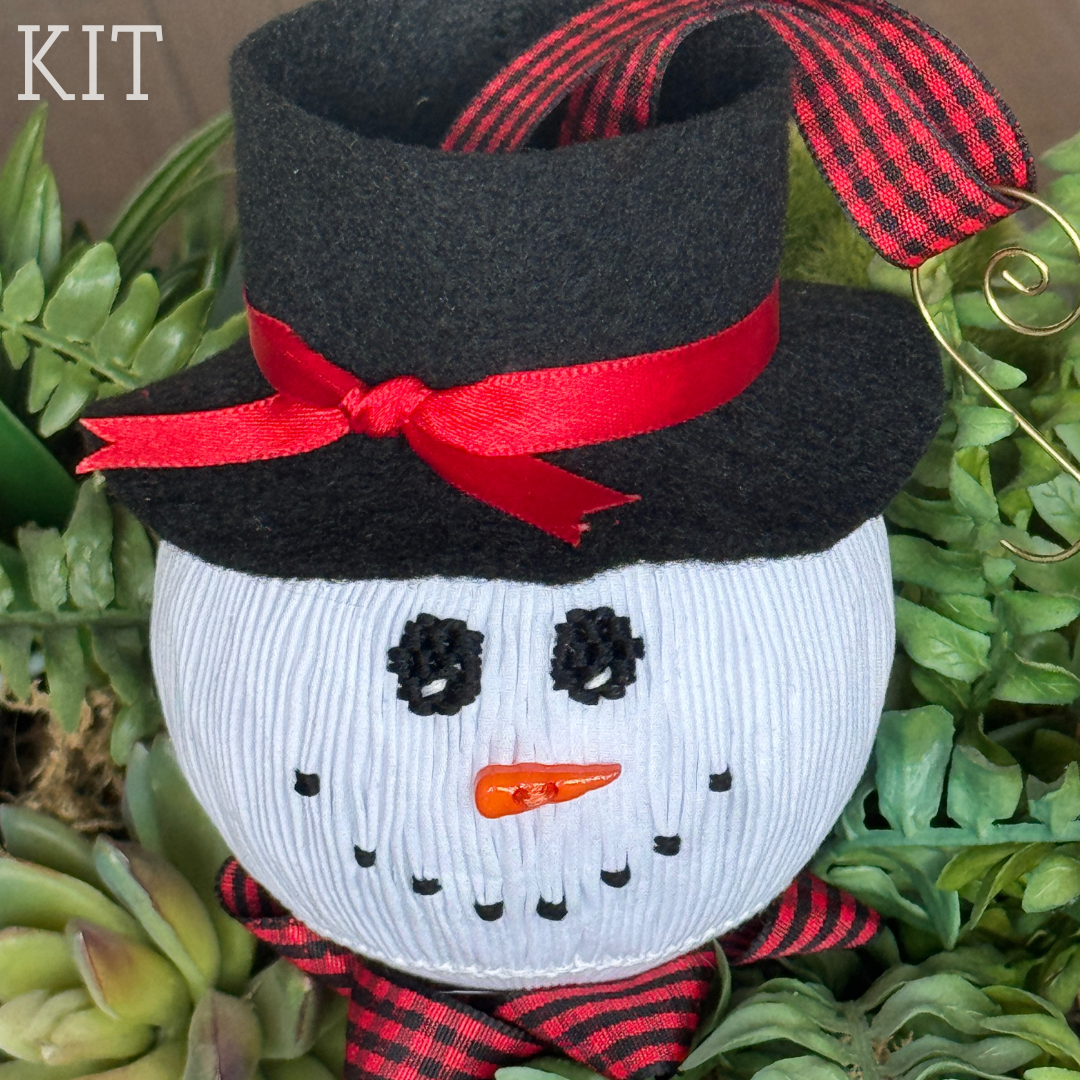 Smocked white snowman ornament with black felt hat, red ribbon bow, and buffalo plaid scarf