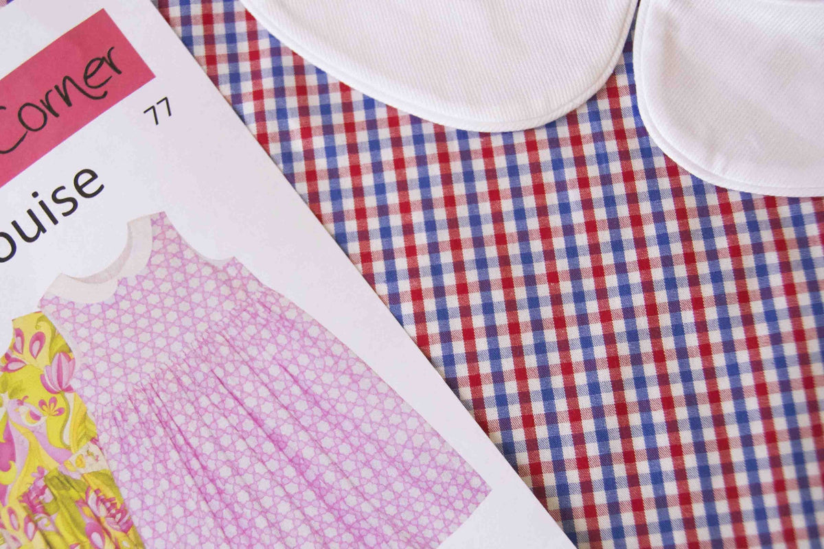 Red, white, and blue gingham check fabric remnant beside a sewing pattern