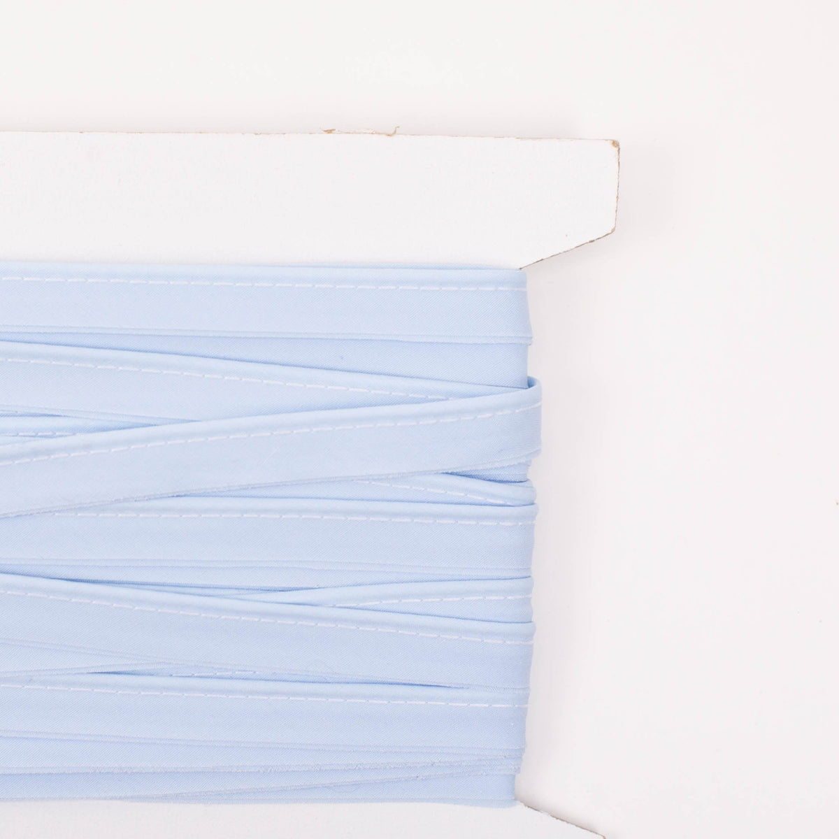 Light blue piping trim wound on a white cardboard card, showing stitched edge detail