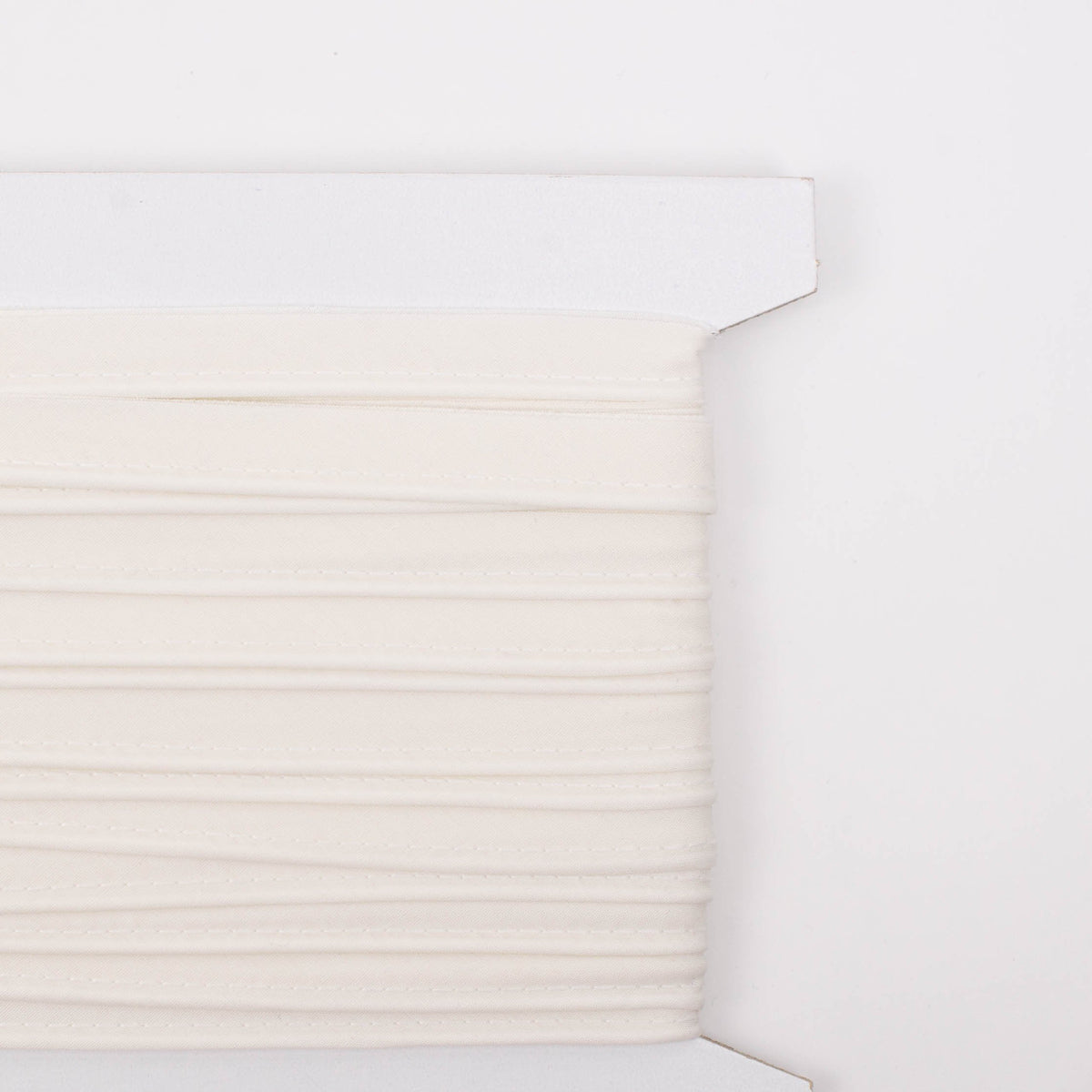 White cotton piping trim wound on a cardboard spool, solid rice color