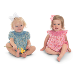 Two baby girls in smocked floral rompers, blue and pink, with hair bows.