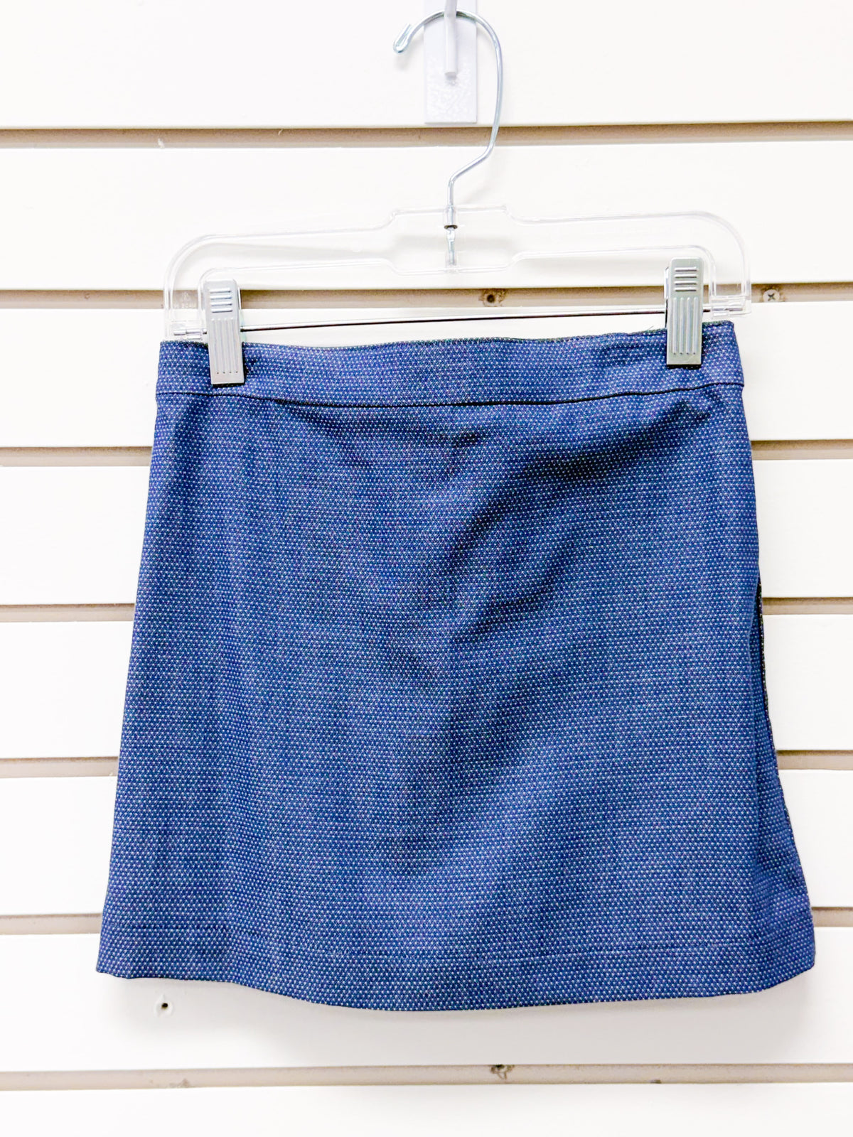 Blue textured mini skort with waistband, displayed on a clear clip hanger