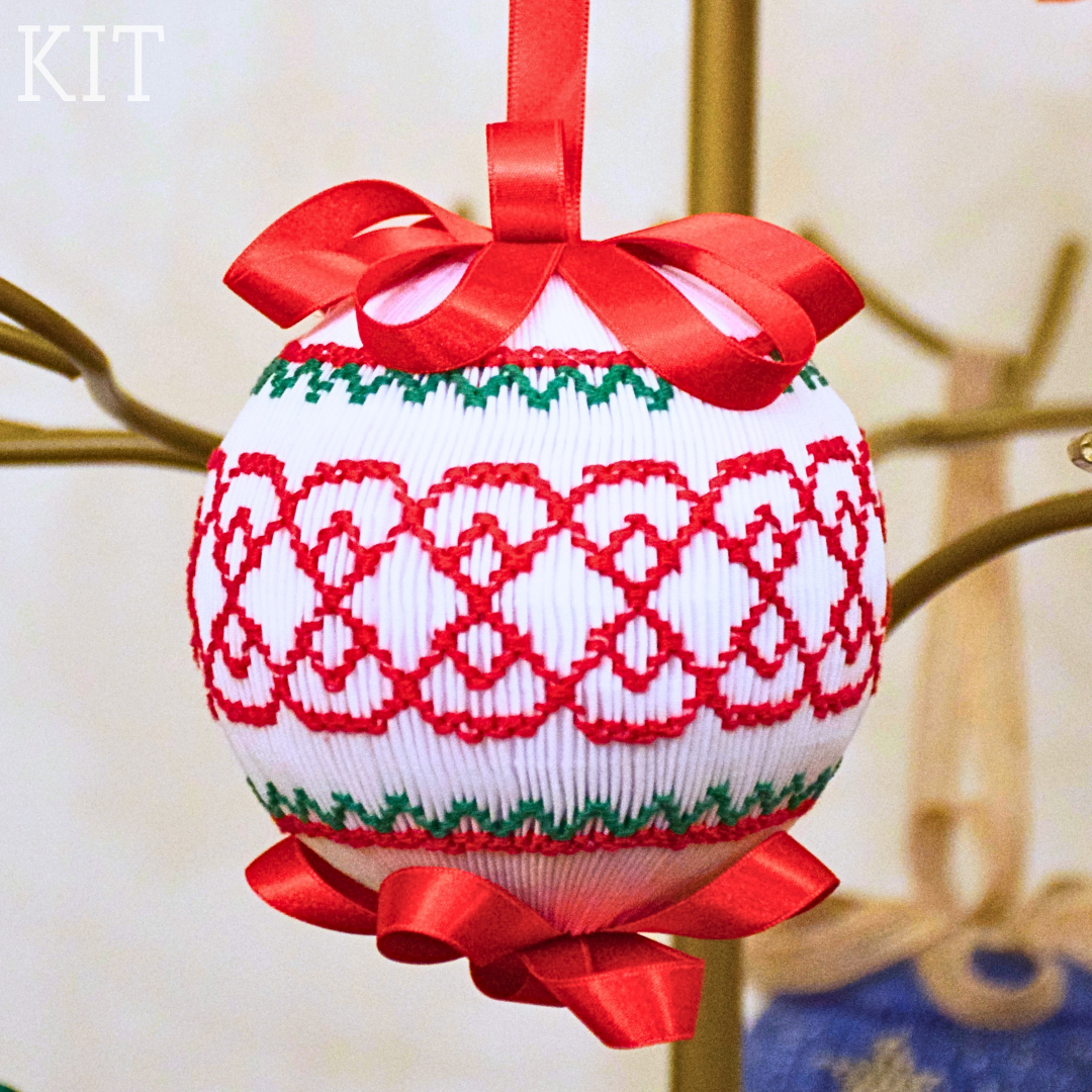 White smocked Christmas ball ornament with red lattice and green trim, red satin bows
