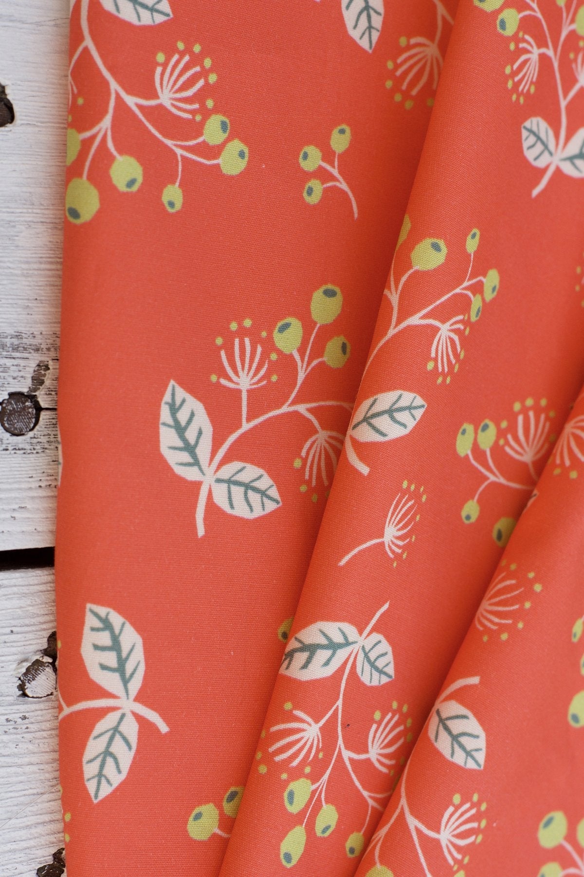 Coral red fabric with white botanical sprigs, green berries, and cream leaves pattern