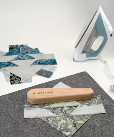 Large wooden clapper tool on felt mat with quilting fabric pieces and iron nearby