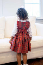Child wearing red and green tartan plaid pinafore dress with white blouse and bow