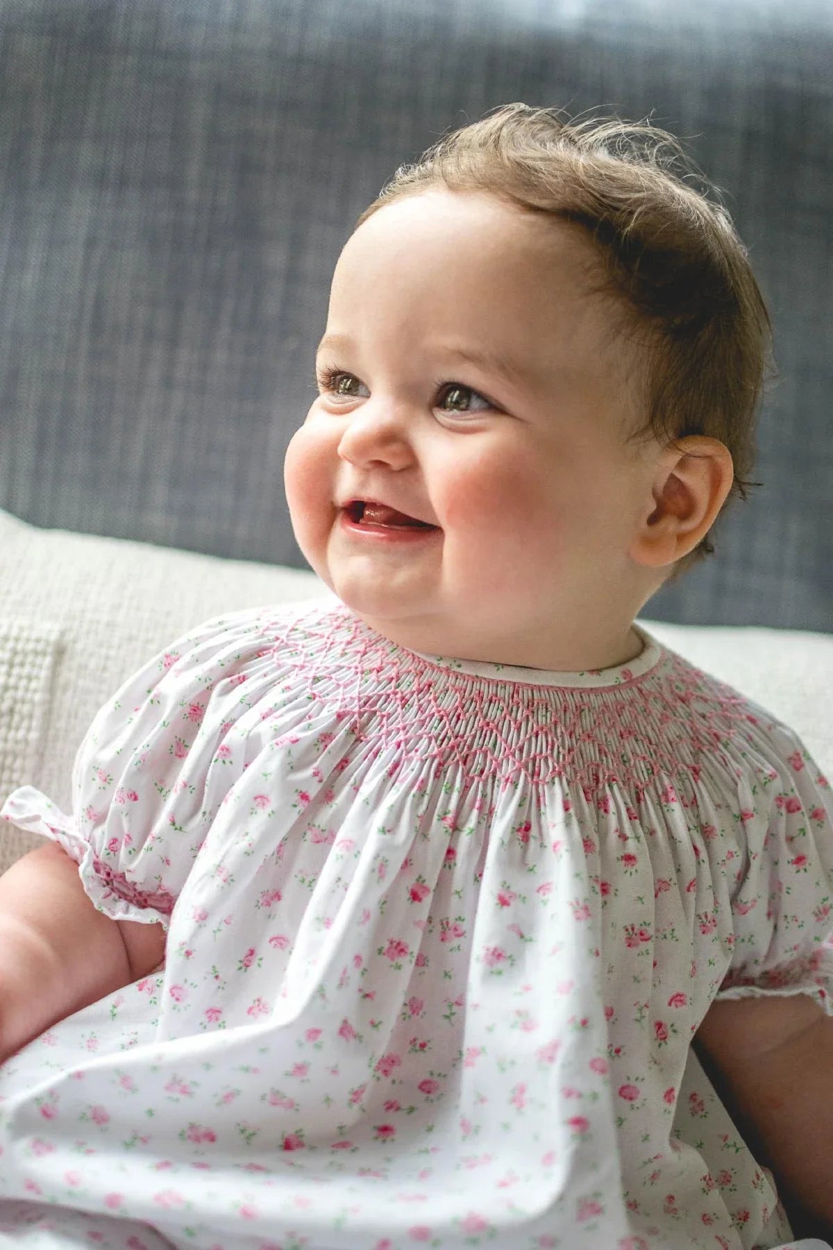 Baby wearing white smocked dress with small pink floral print, rosy pink roses pattern