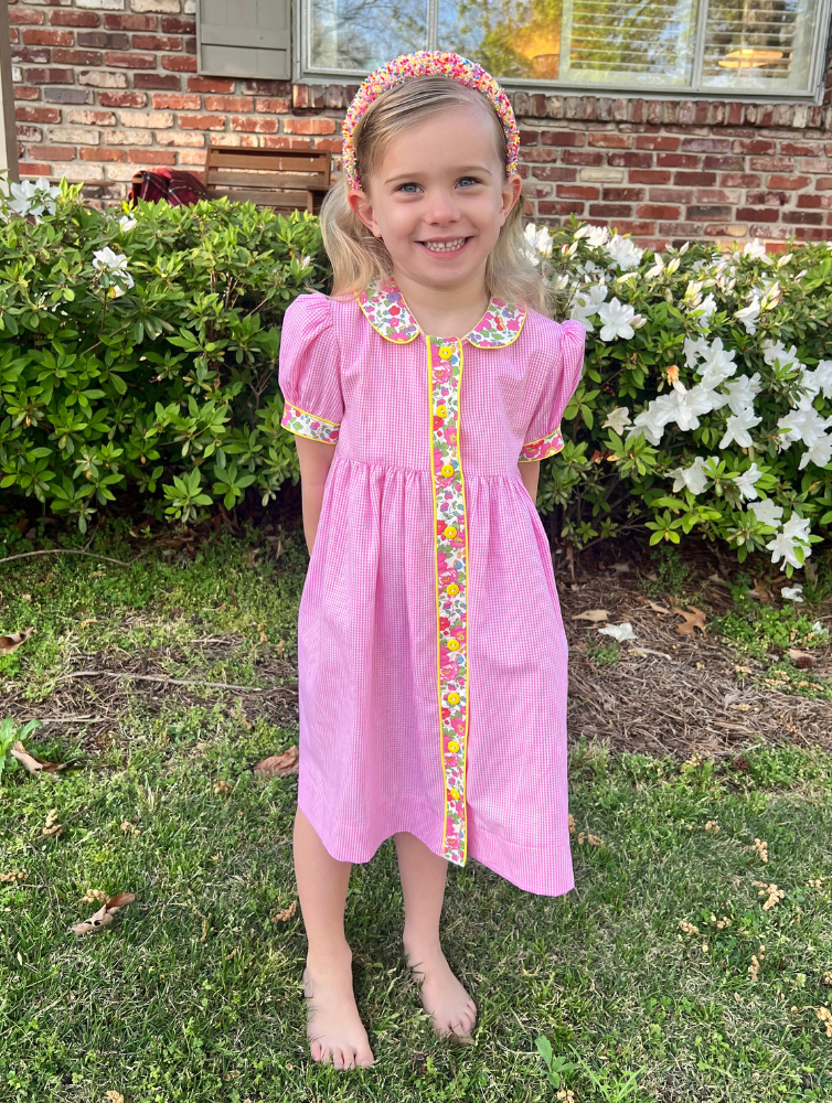 Girl wearing pink gingham dress with floral trim, Peter Pan collar, and puff sleeves