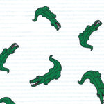 White fabric with blue stripes and scattered green cartoon alligator print pattern