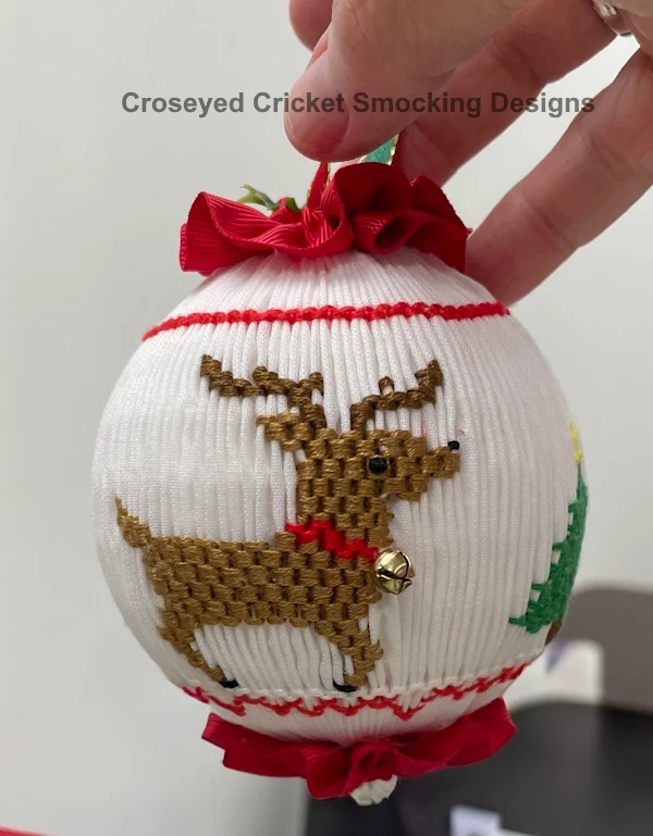 Smocked white Christmas ornament ball with embroidered reindeer, red ribbon bow and trim