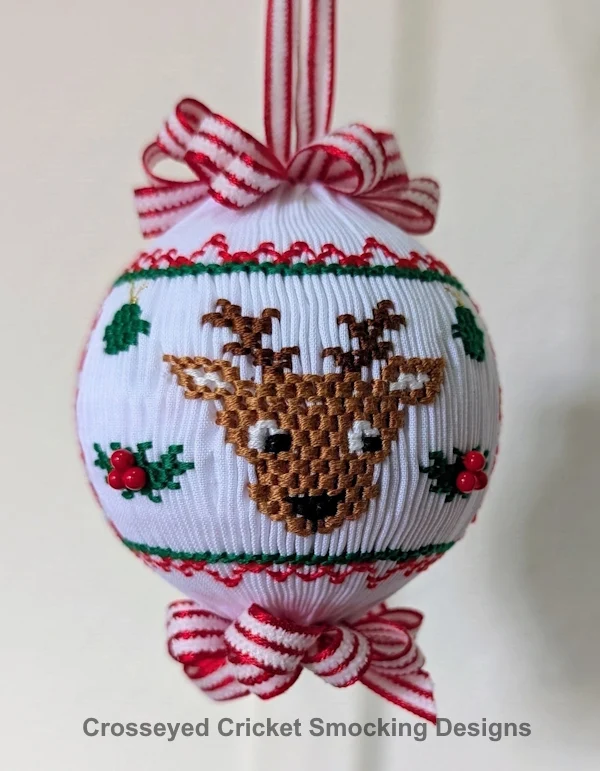 Smocked white Christmas ornament with embroidered reindeer, holly, and red ribbon bows