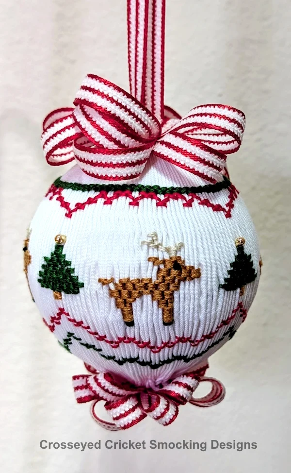 White smocked Christmas ornament ball with reindeer and trees, red ribbon bow