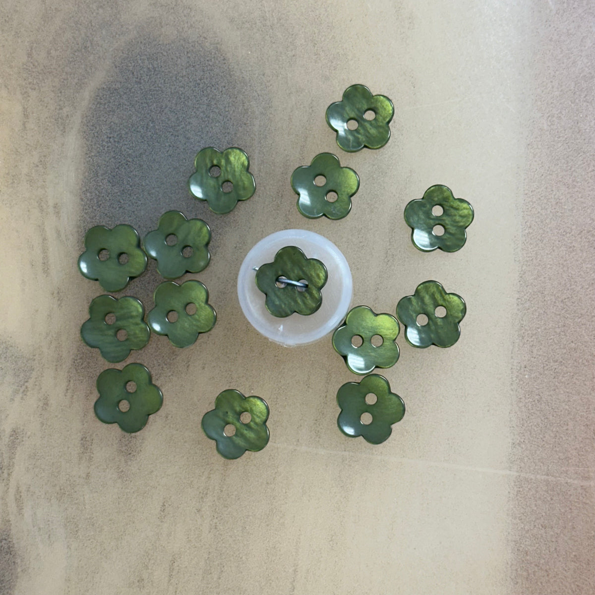 Green pearlescent flower-shaped plastic buttons with two holes, arranged in a circle
