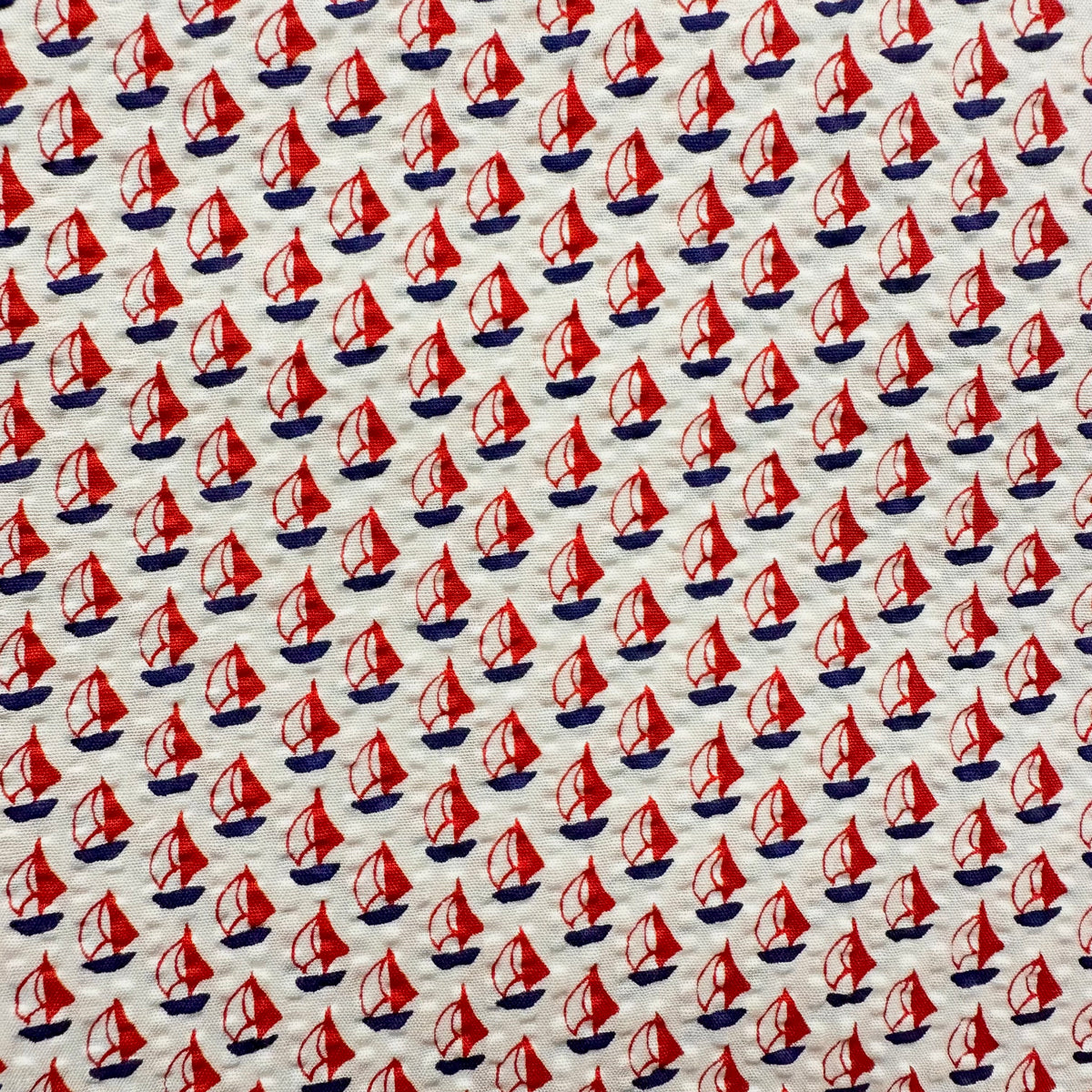 White seersucker fabric with red sailboat print and navy blue hulls pattern