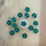 Teal green flower-shaped two-hole plastic buttons arranged in a circle on wood surface