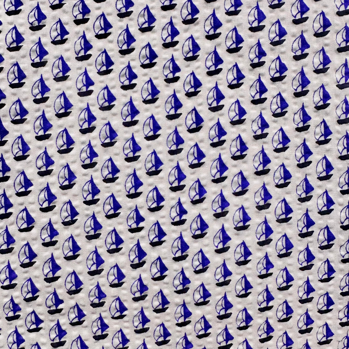 White seersucker fabric with repeating small royal blue sailboat print pattern