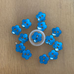 Blue flower-shaped plastic buttons with two holes, arranged in a circle on wood surface