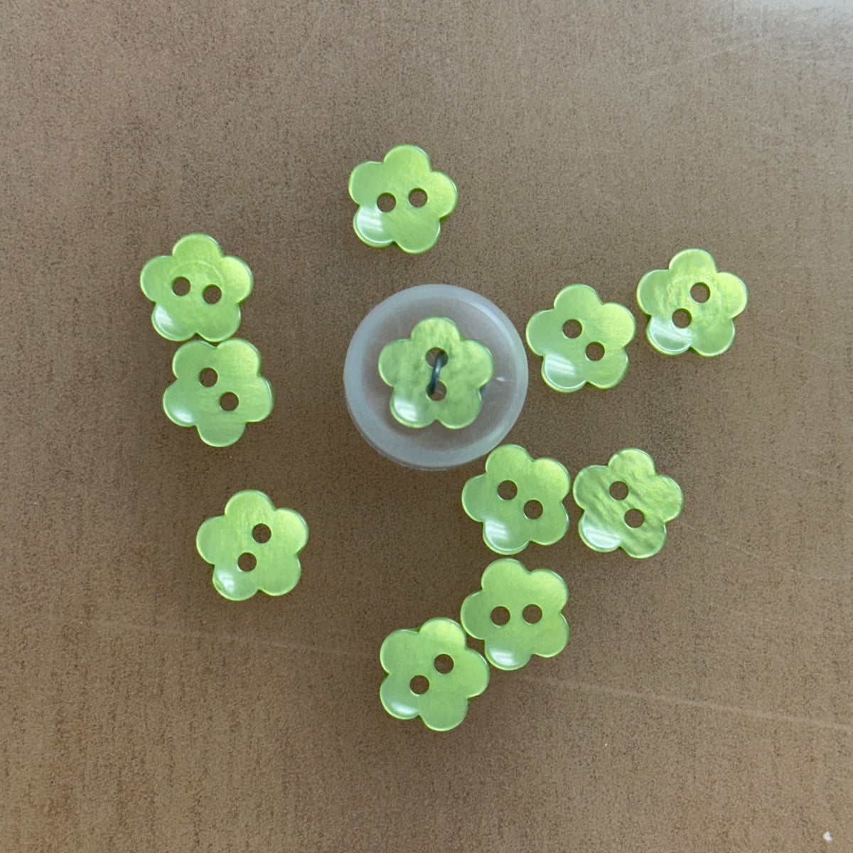 Lime green flower-shaped 2-hole plastic buttons, half-inch size, shown on tan background