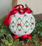 White smocked Christmas ornament with green diamond pattern, red bow accents, and satin ribbon