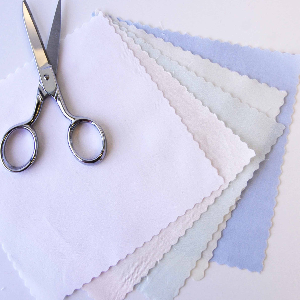 Scallop-edged champagne pima batiste fabric swatches fanned out beside silver scissors