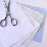 Scallop-edged champagne pima batiste fabric swatches fanned out beside silver scissors
