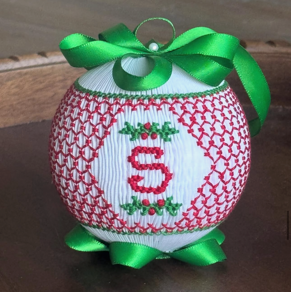 White smocked Christmas ornament with red embroidered letter S and green satin bow