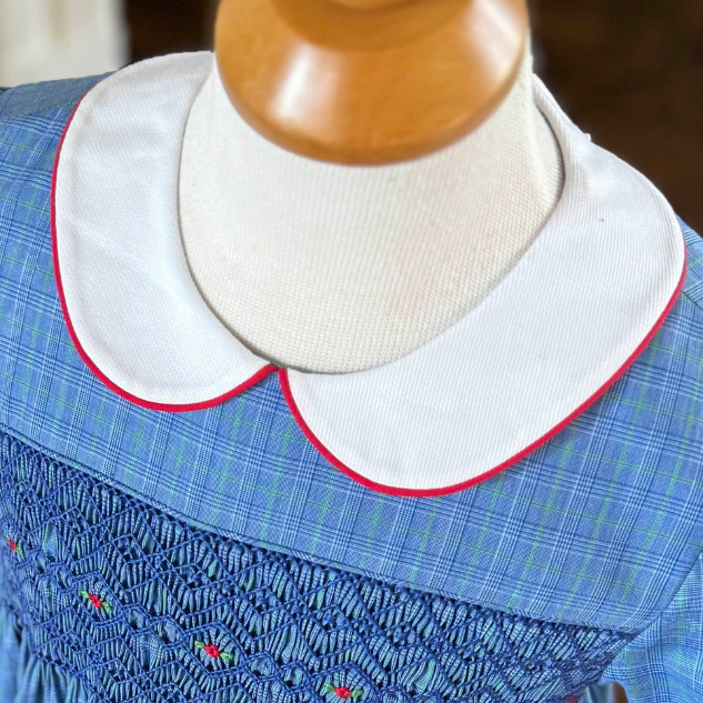 White pique peter pan collar with red piping on blue smocked dress form
