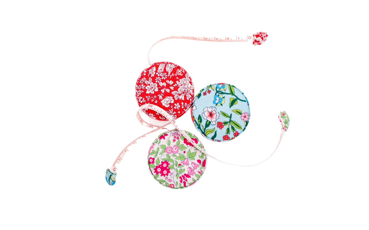 Three floral Liberty fabric retractable tape measures in red, blue, and pink patterns.