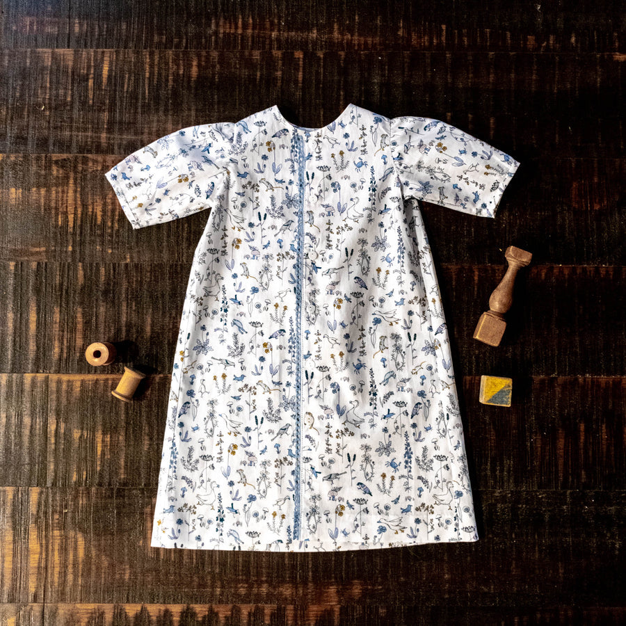 White Liberty fabric children's dress with blue floral and bird print, flat lay