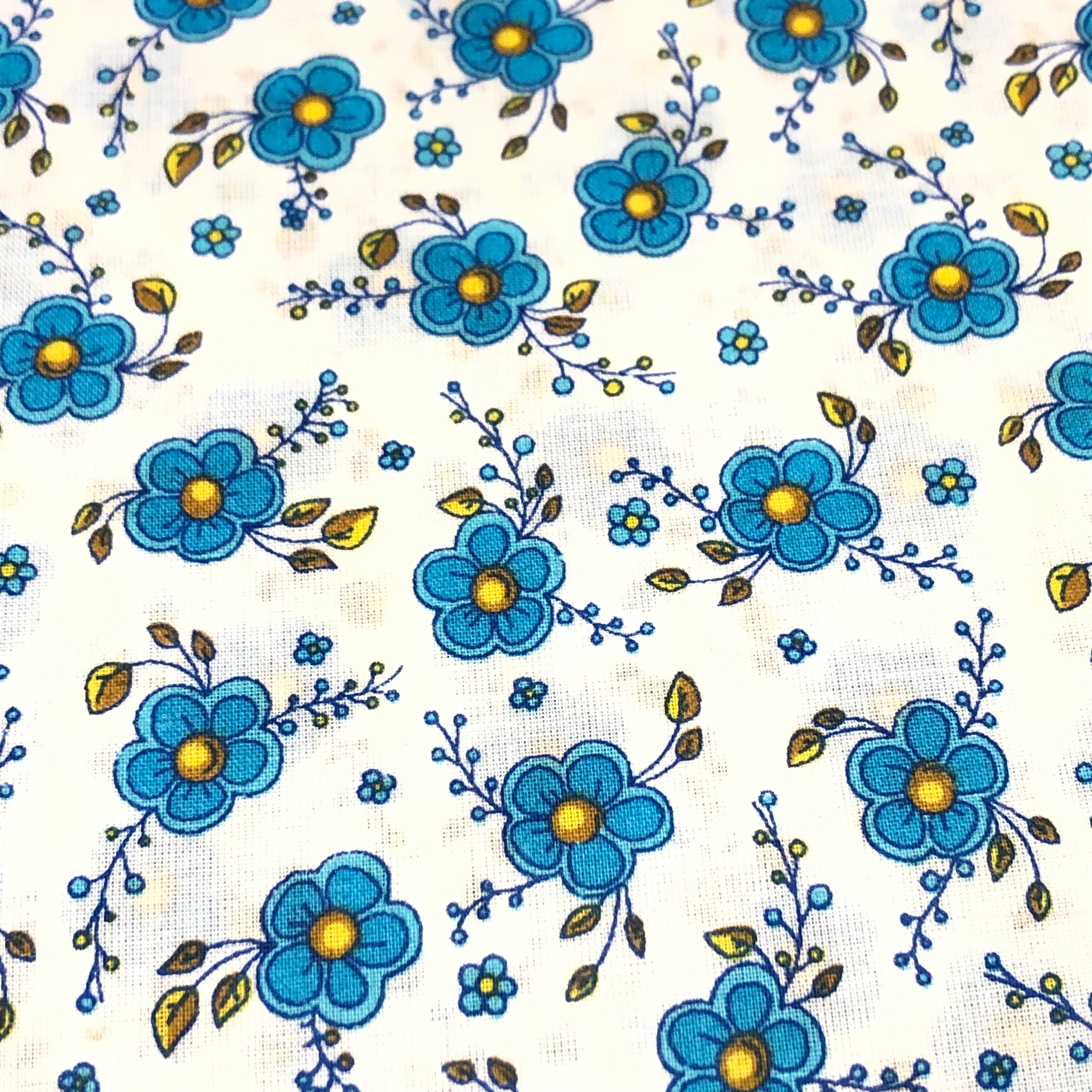 White cotton lawn fabric with blue floral print, yellow centers, and brown leaf accents