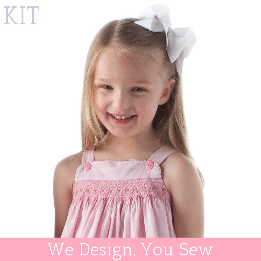 Girl wearing pink smocked sundress with button straps and white hair bow